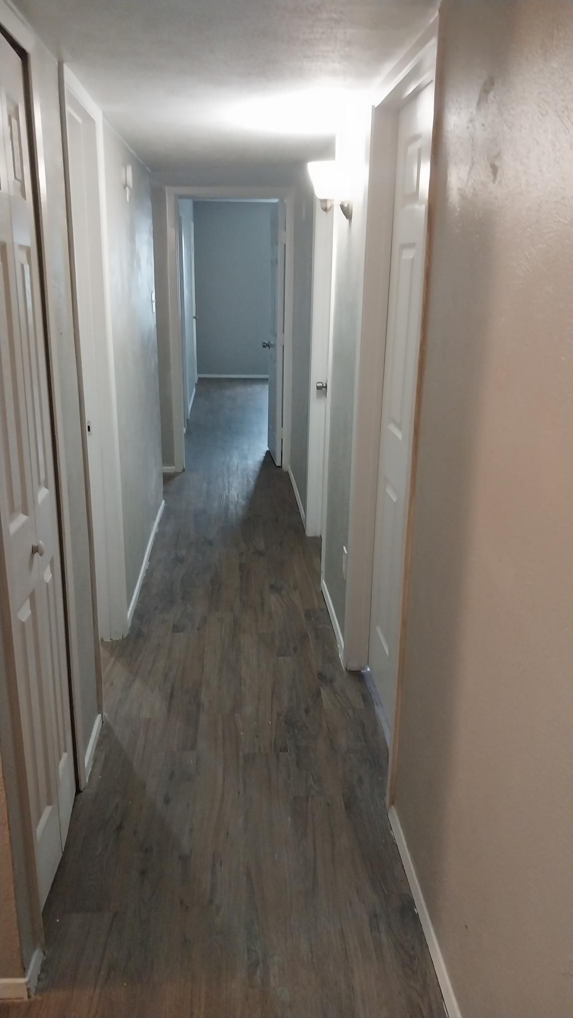 Long hallway with doors, gray wood-look floor, and light beige walls.