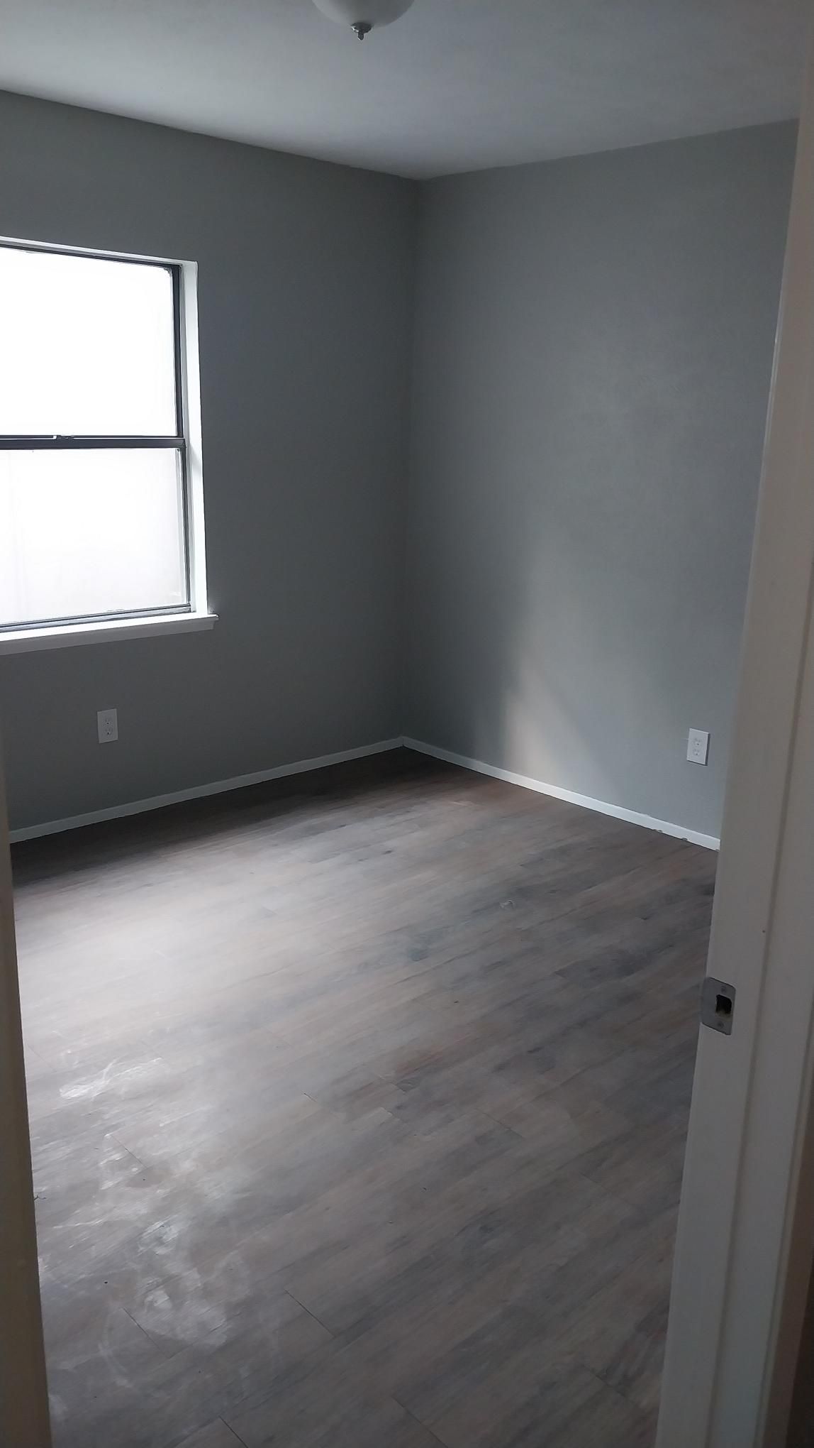 Empty room with gray walls, dark wood-look floor, and a window.