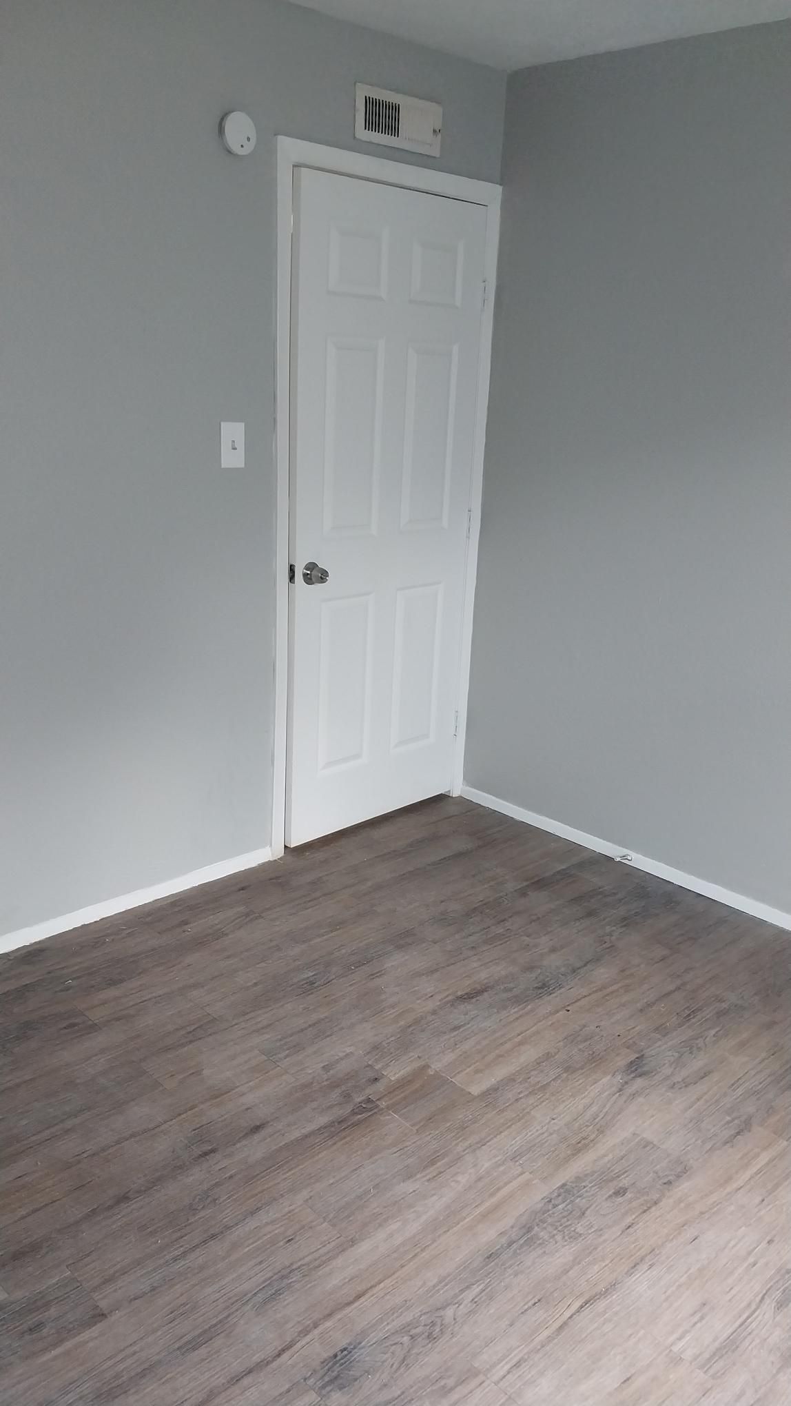Empty room with gray walls, white door, and wood-look flooring.