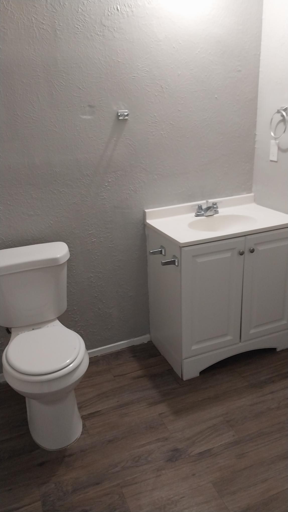 Bathroom with white toilet, vanity, and silver fixtures. Gray walls, brown flooring.
