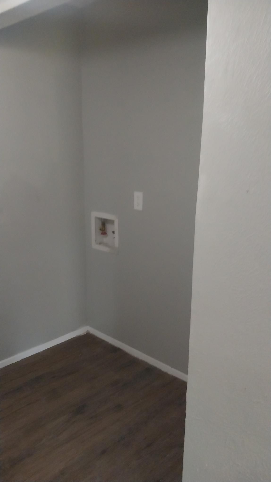 Empty laundry room with gray walls, brown flooring, and water hookups.