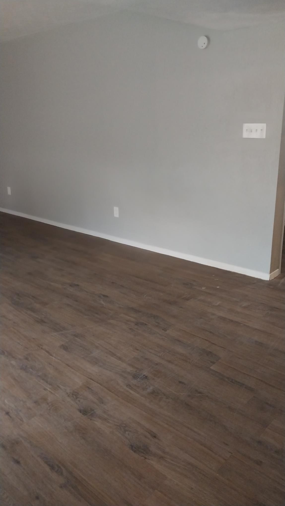 Empty room with gray walls, dark wood-look flooring, and white trim.