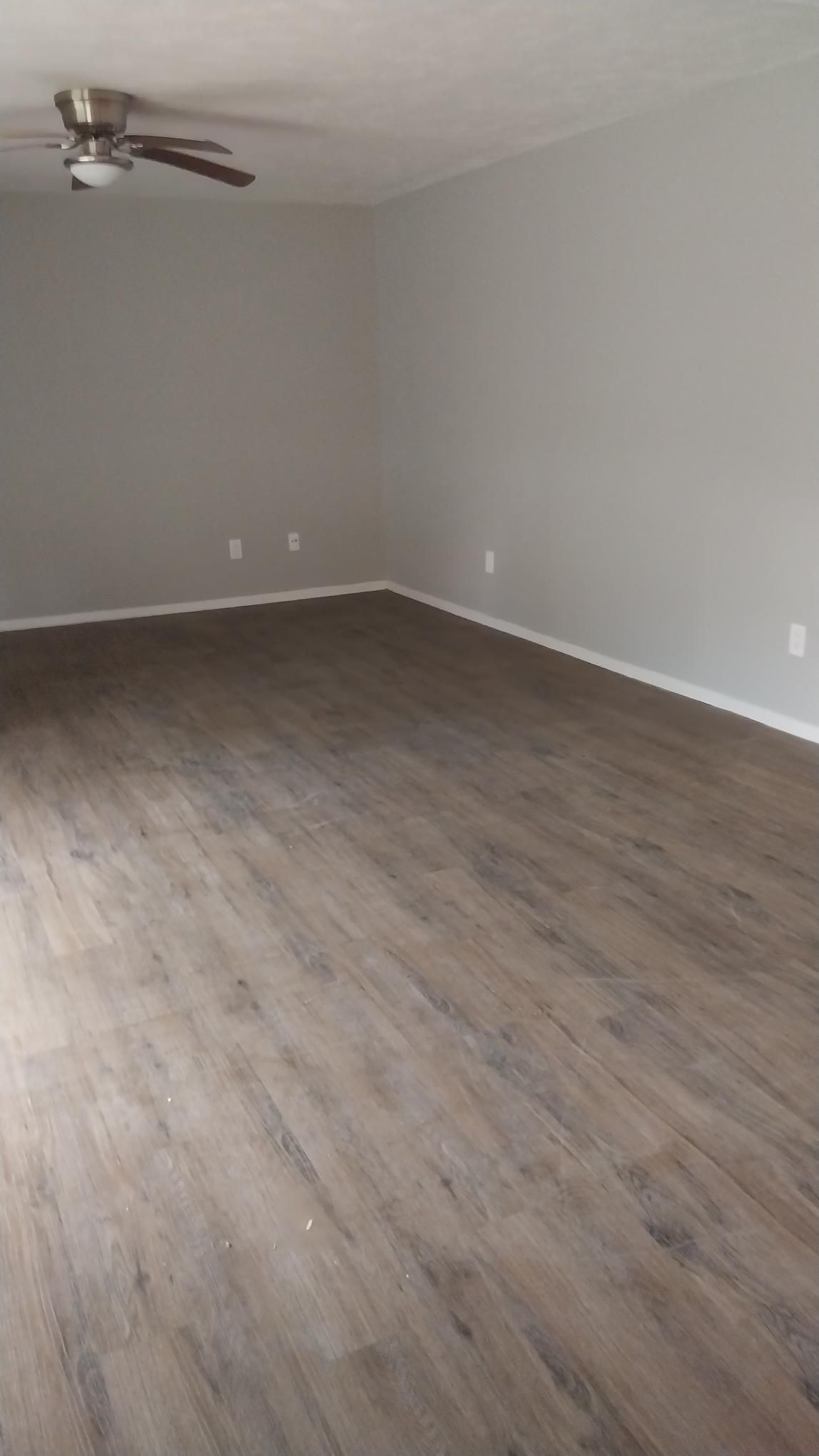 Empty room with gray walls, wood-look flooring, and ceiling fan.