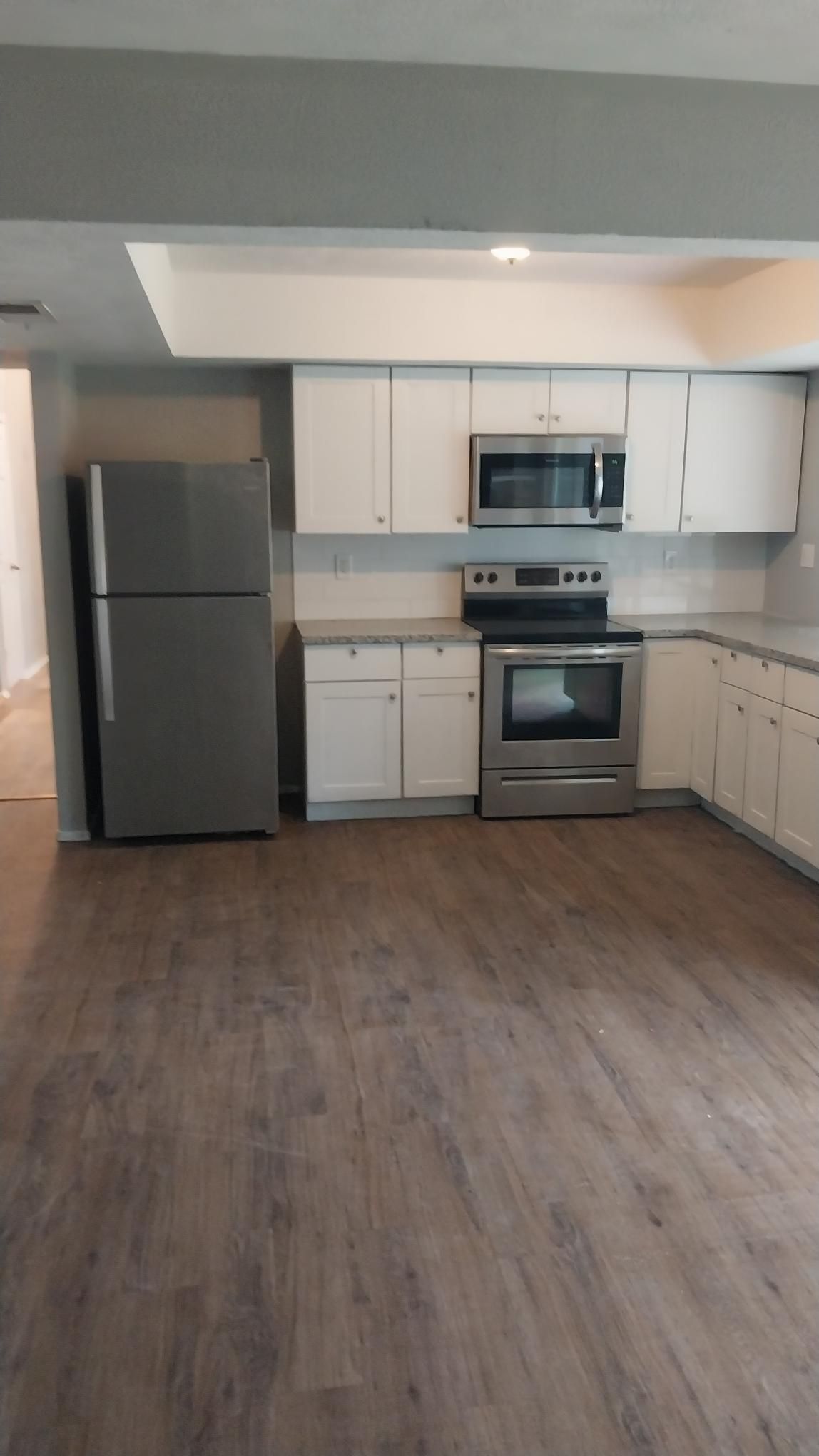 Modern kitchen with white cabinets, stainless steel appliances, gray countertop, and wood-look flooring.