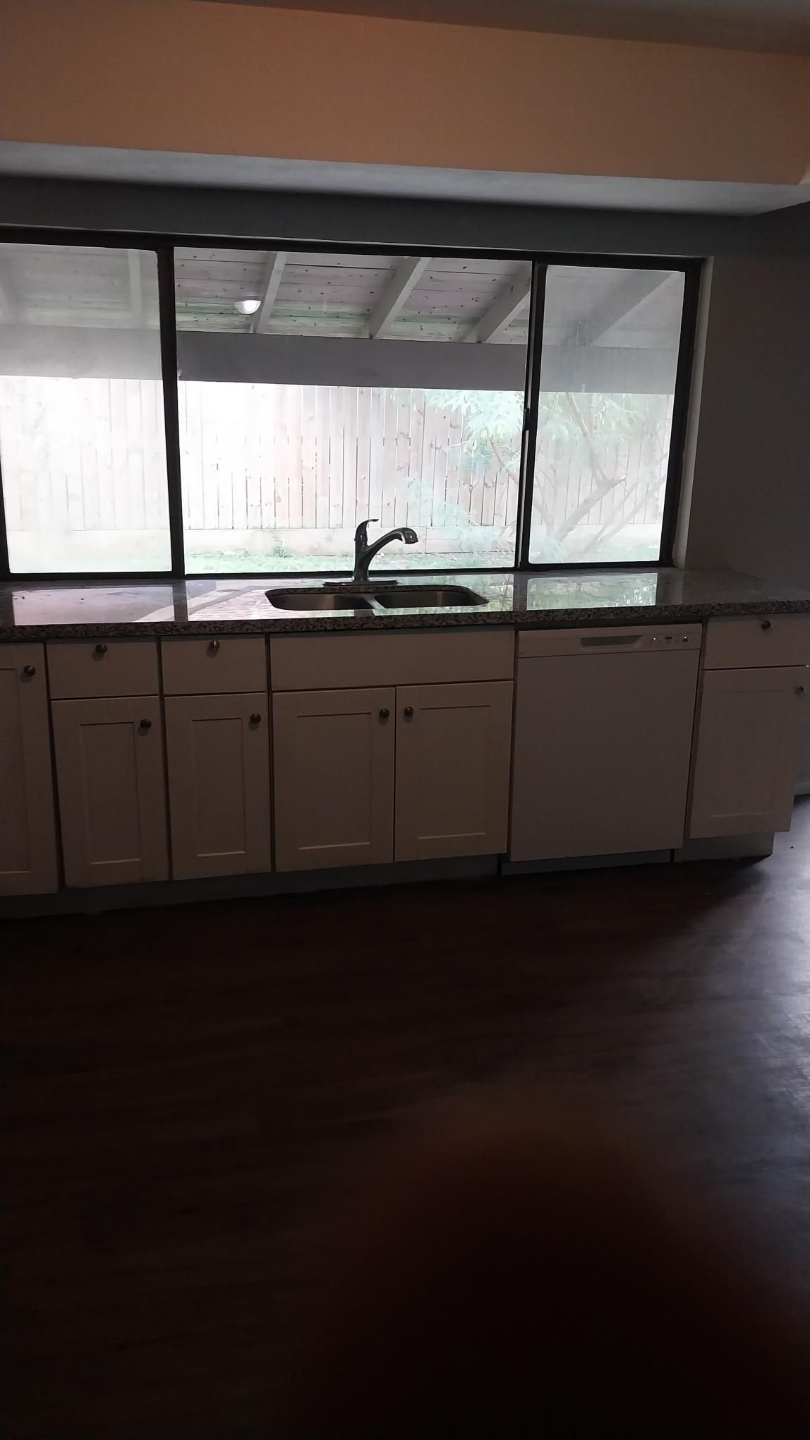 Kitchen with white cabinets, dark countertops, sink, and large window overlooking trees.