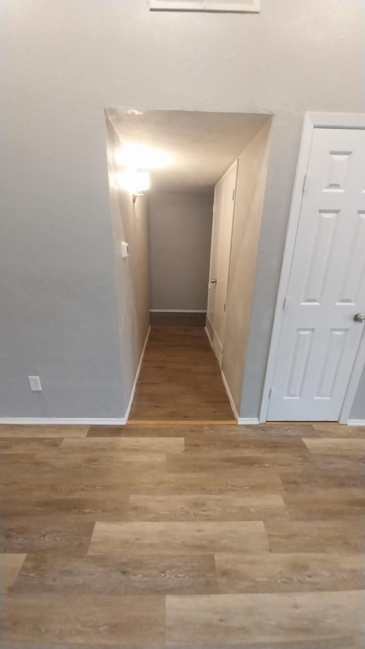 Narrow hallway with gray walls, wooden floor, and white doors. Recessed lighting.