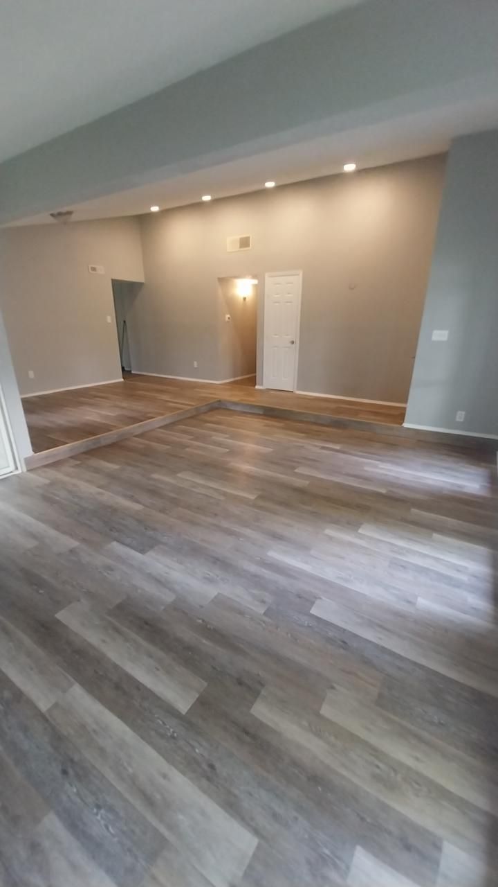 Empty room with gray-toned wood flooring and gray walls; doorways visible, recessed lighting.
