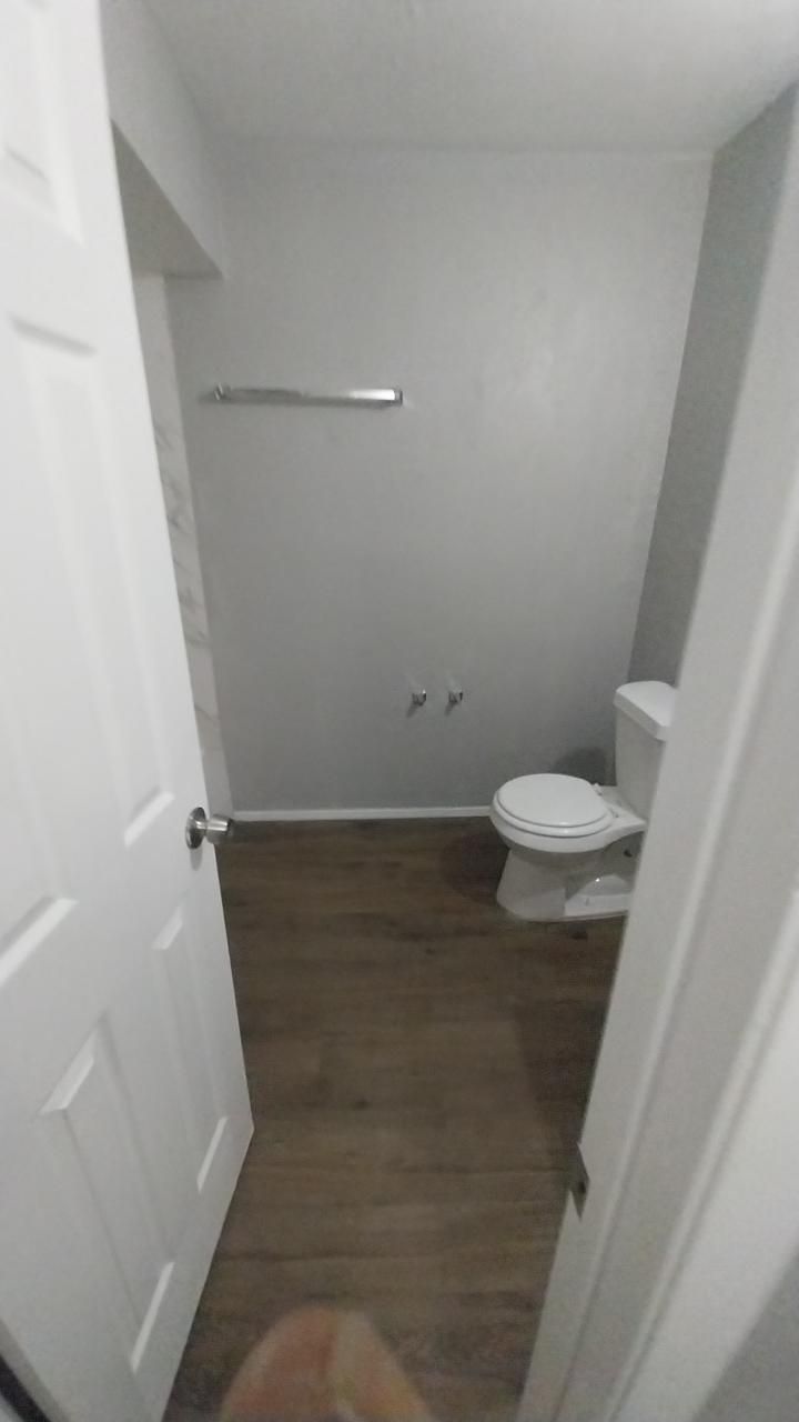 Bathroom with a white toilet, gray walls, and wood-look flooring. A towel rack is on the wall.