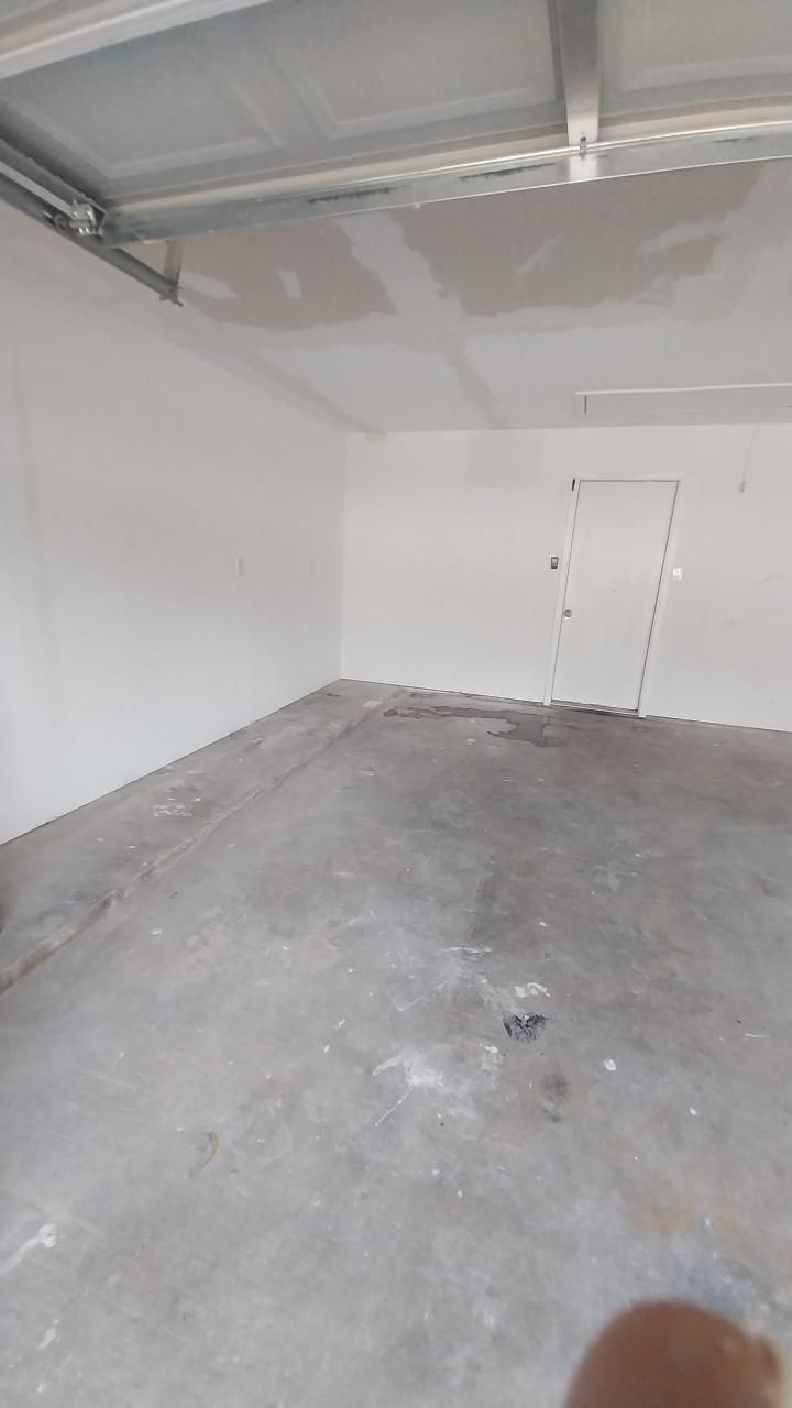 Empty garage with white walls, a concrete floor, and a closed door.