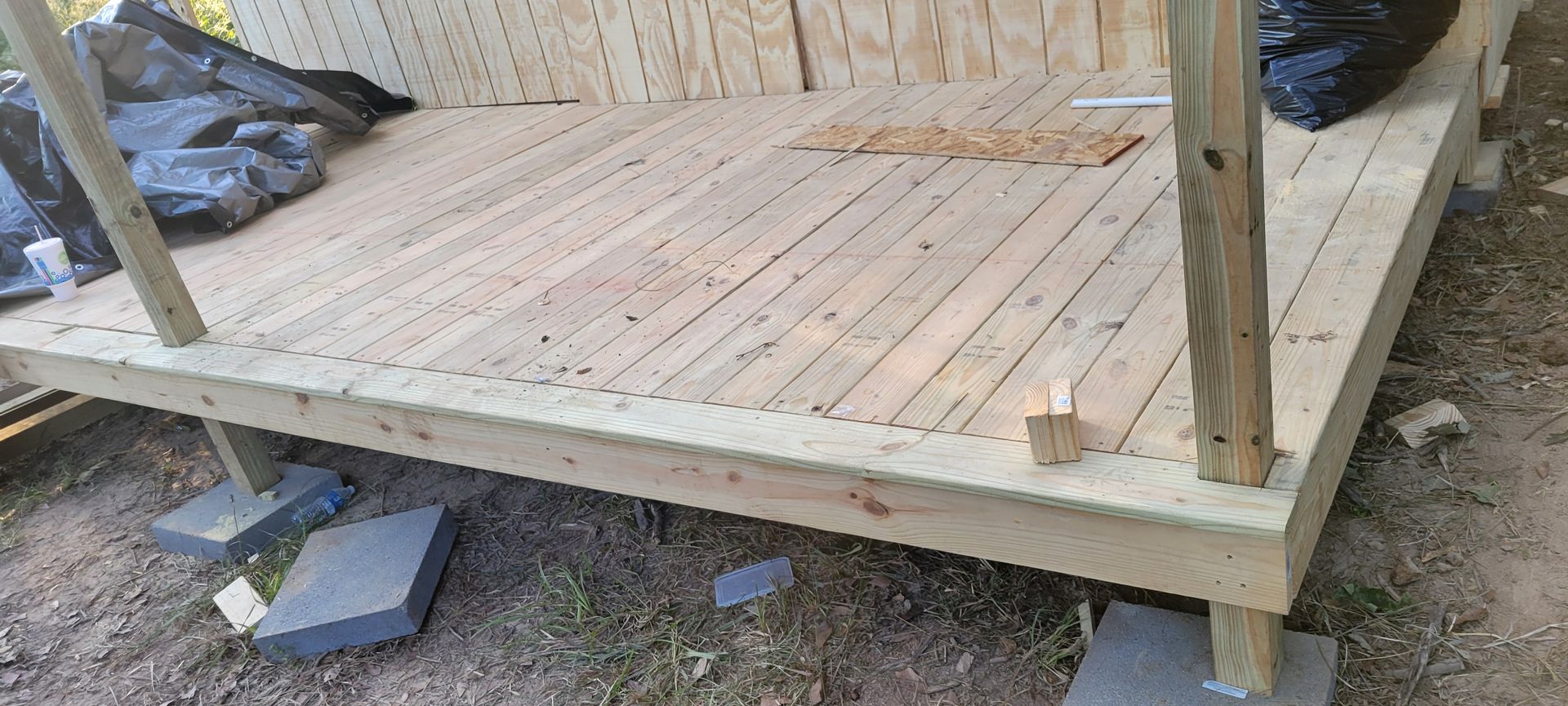 A partially built wooden deck with support posts and concrete blocks sitting on a grassy area.