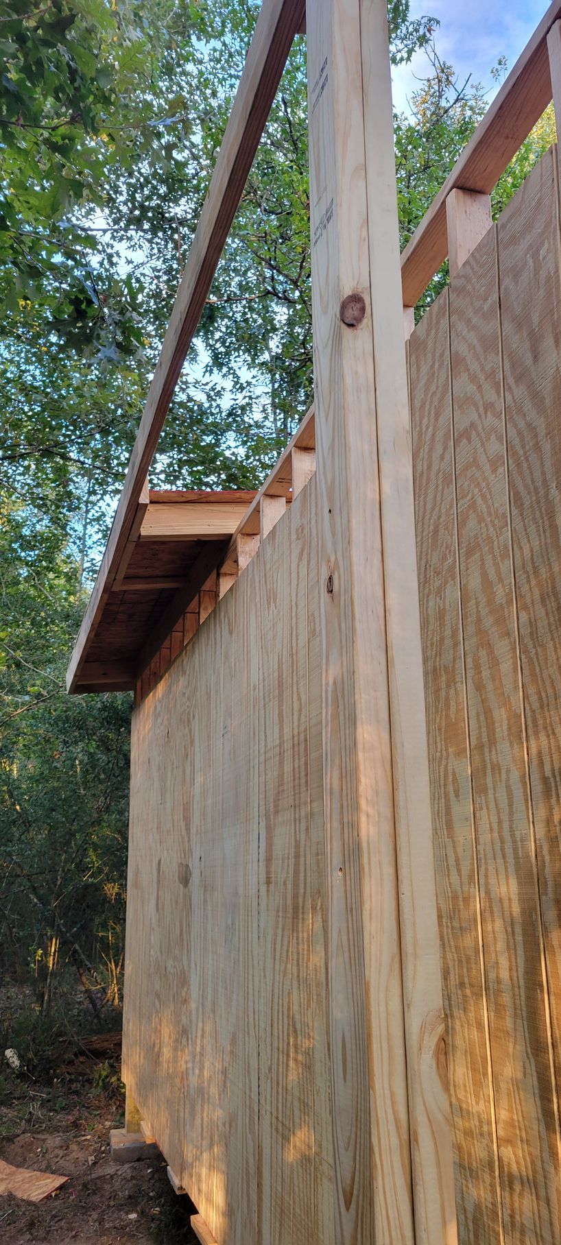 Wooden structure under construction, partially built with plywood siding. A beam extends over the top.