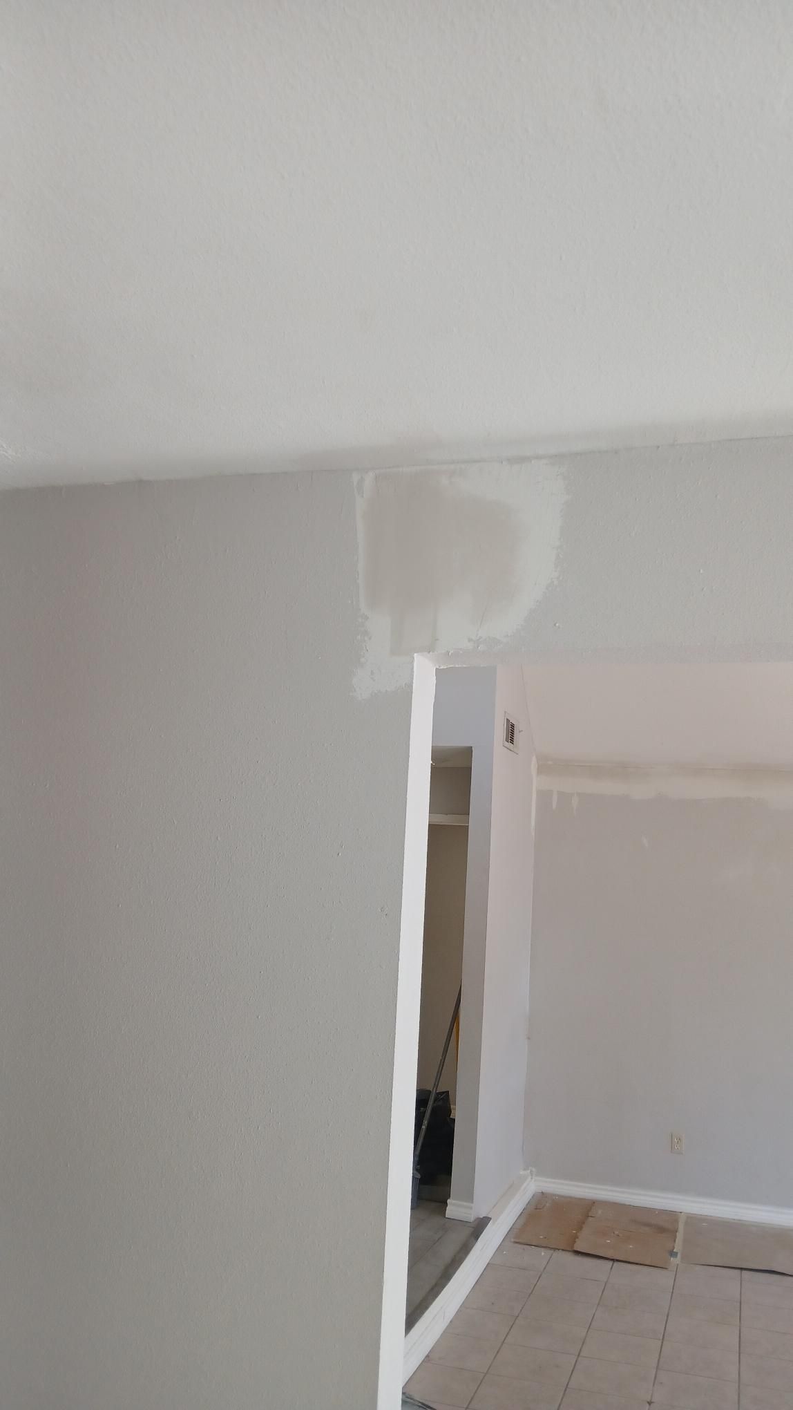 Repaired drywall patch on a wall, transition to a hallway, with white and gray paint.