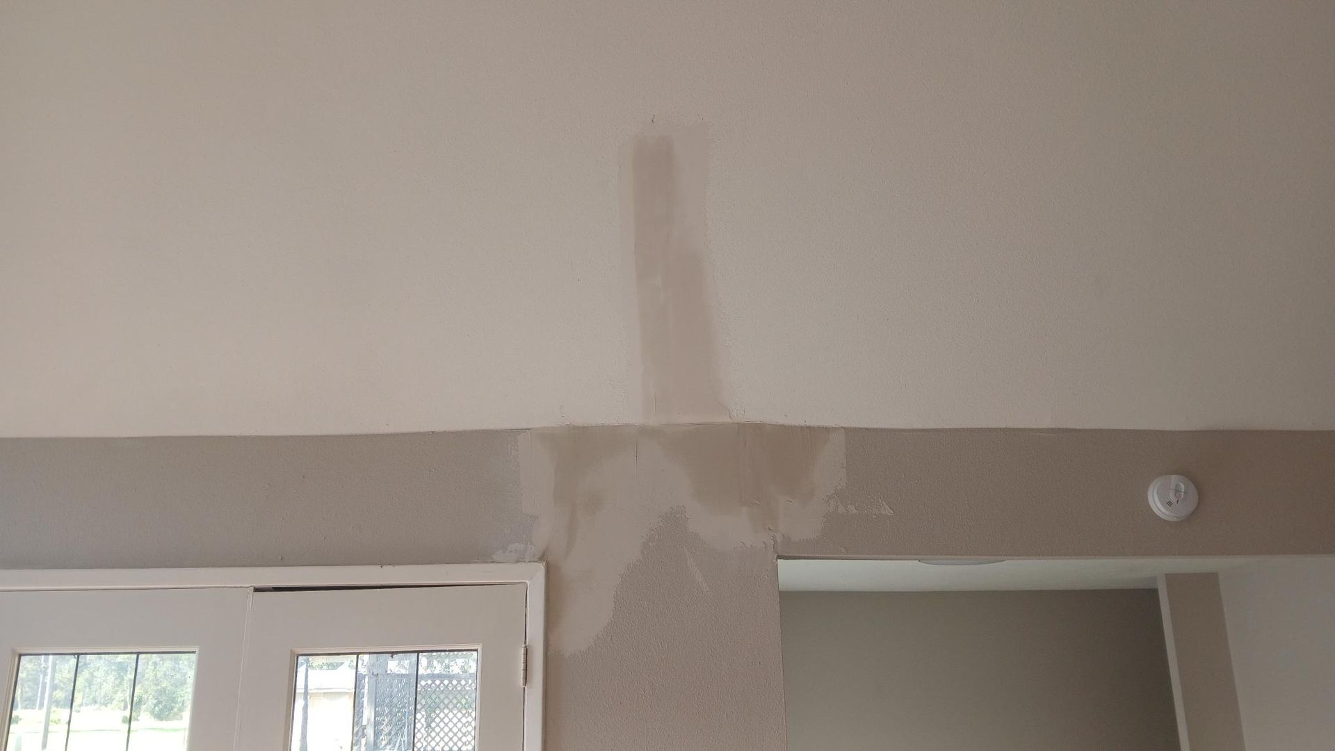 Beige ceiling and wall with visible patching and repairs; a door frame is visible.