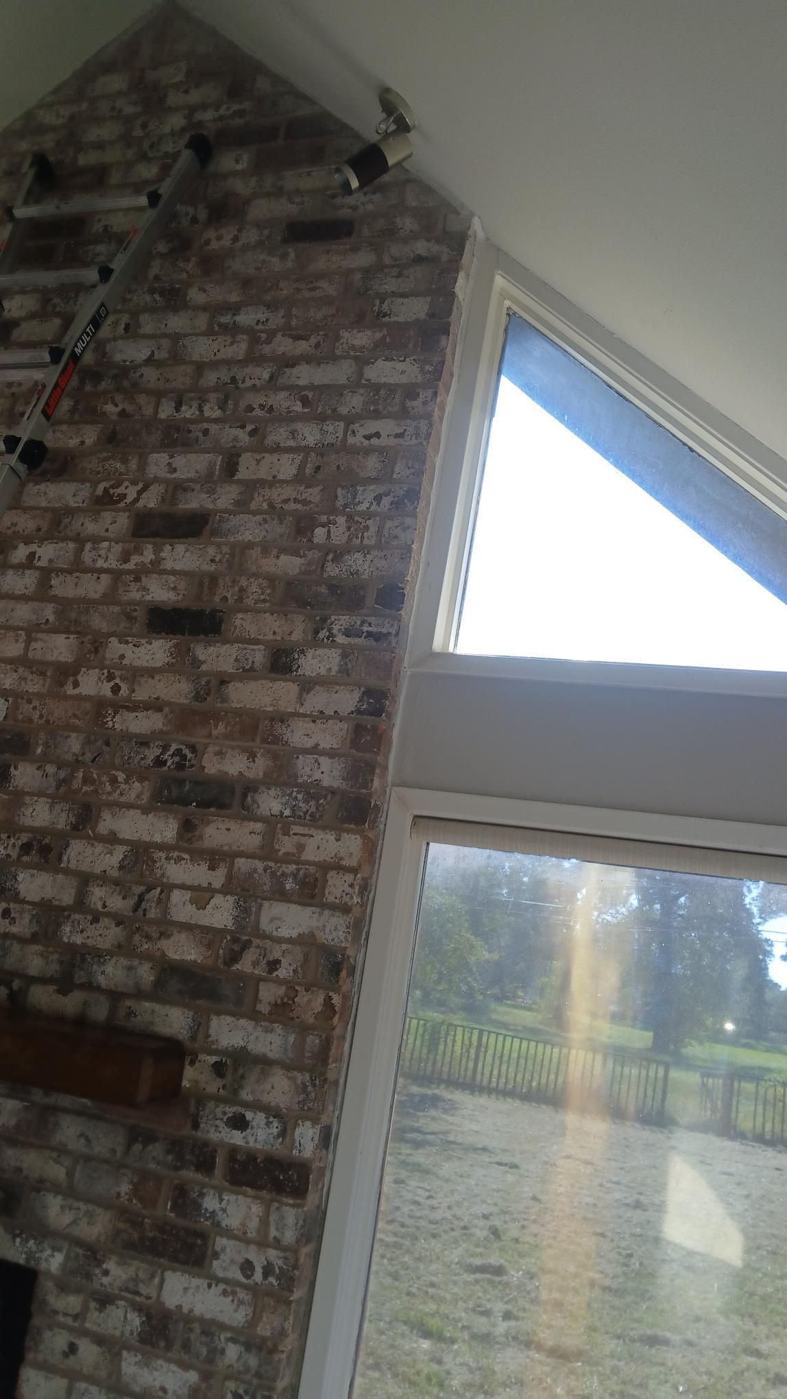 Brick fireplace beside a large window with outdoor view, lit by sunlight.