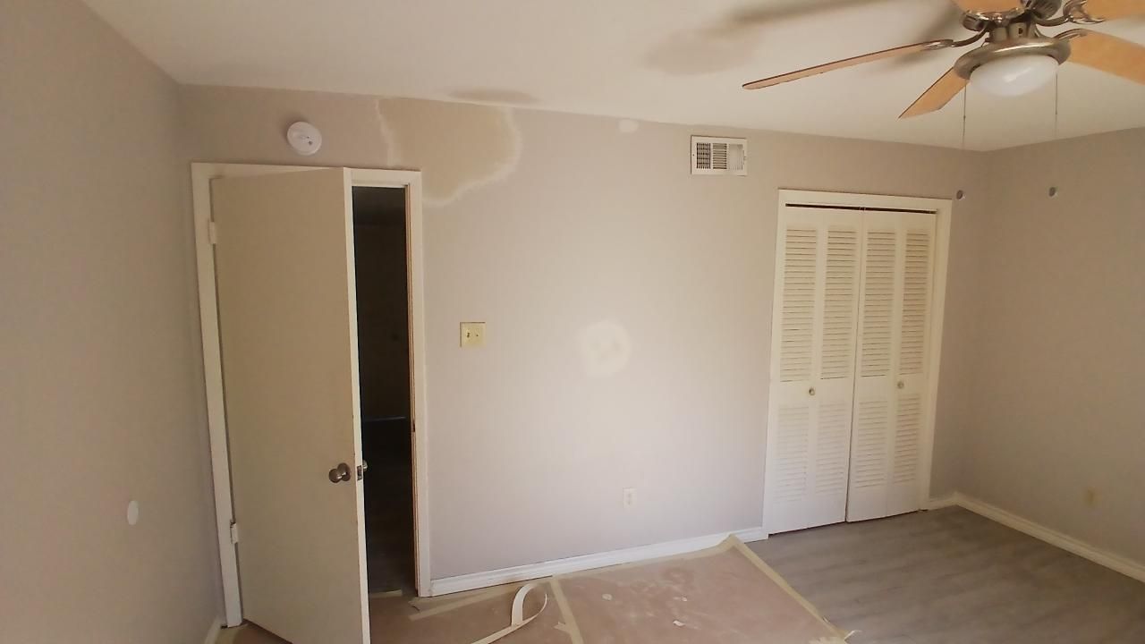 Bedroom with beige walls, two doors, closet, and ceiling fan. Some wall damage is visible.