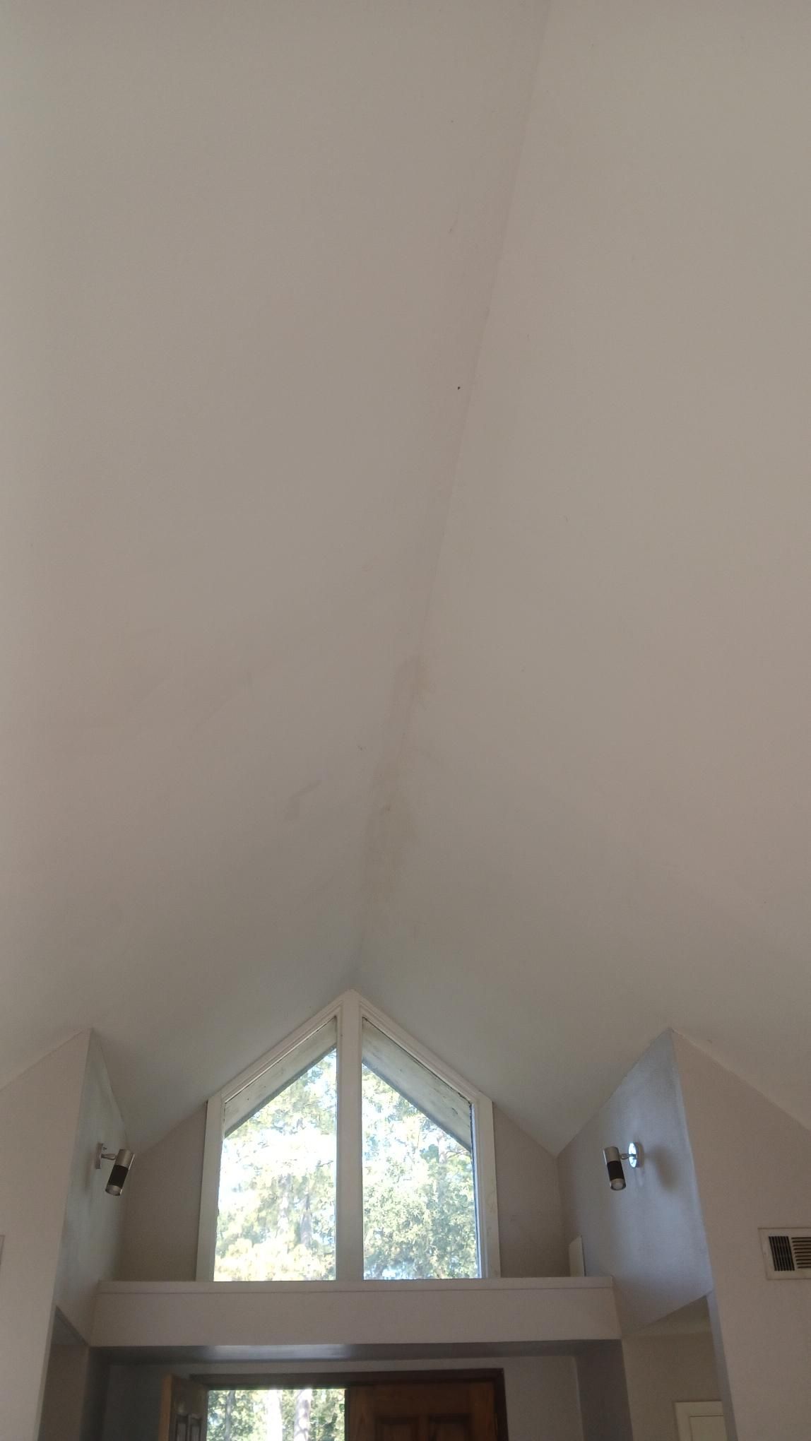 White vaulted ceiling with a large triangular window, small shelf, and sconces.