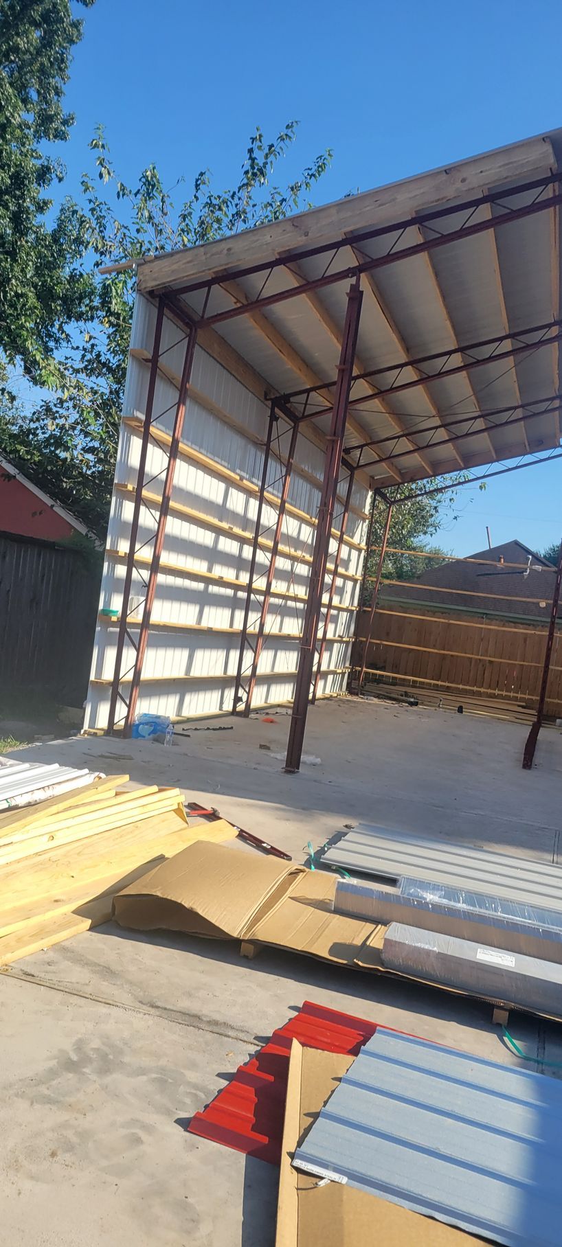 A partially constructed metal and wood carport under a blue sky, with building materials scattered nearby.