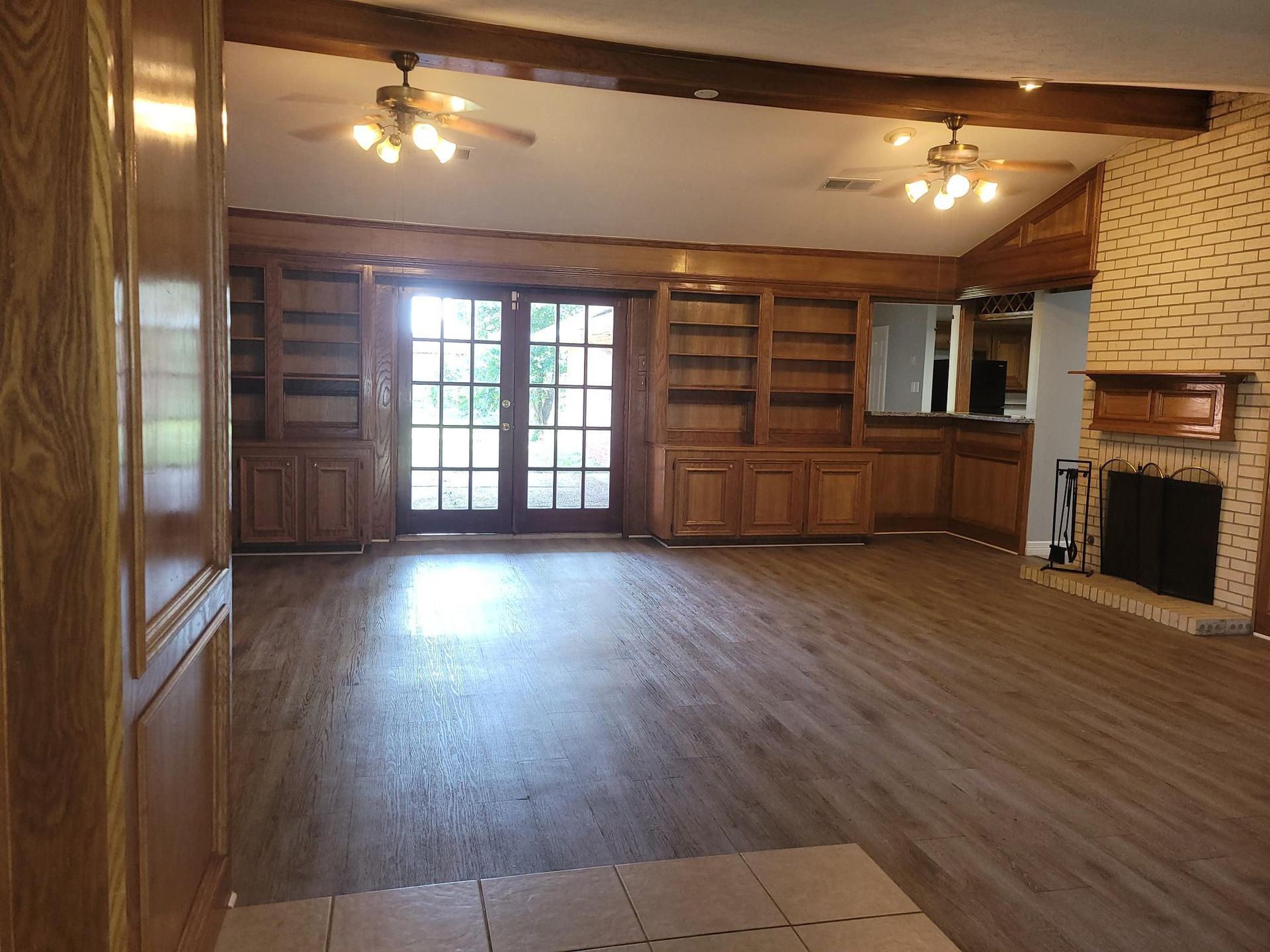 Spacious living room with wood flooring, built-in shelves, French doors, and a brick fireplace.