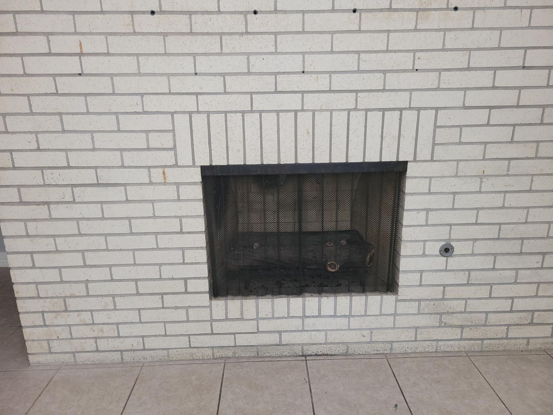 White brick fireplace with dark interior and a black metal screen.