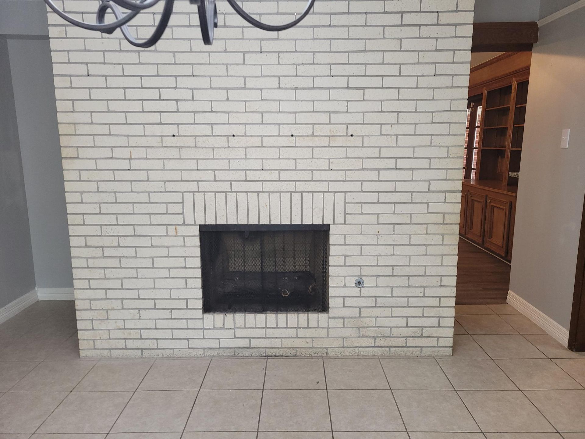 White brick fireplace with black insert, tiled floor, and doorway to a wooden bookshelf.