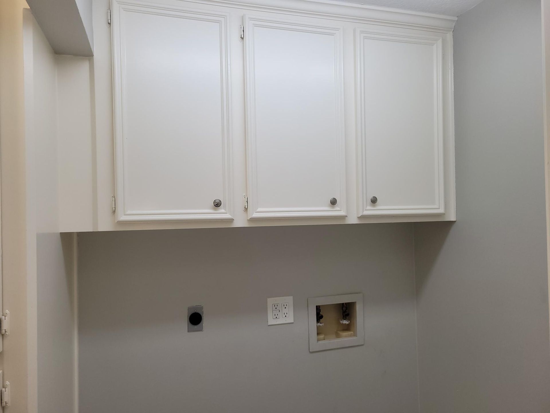 Laundry room with white cabinets above a gray wall. Electrical outlets and a water hookup are visible.