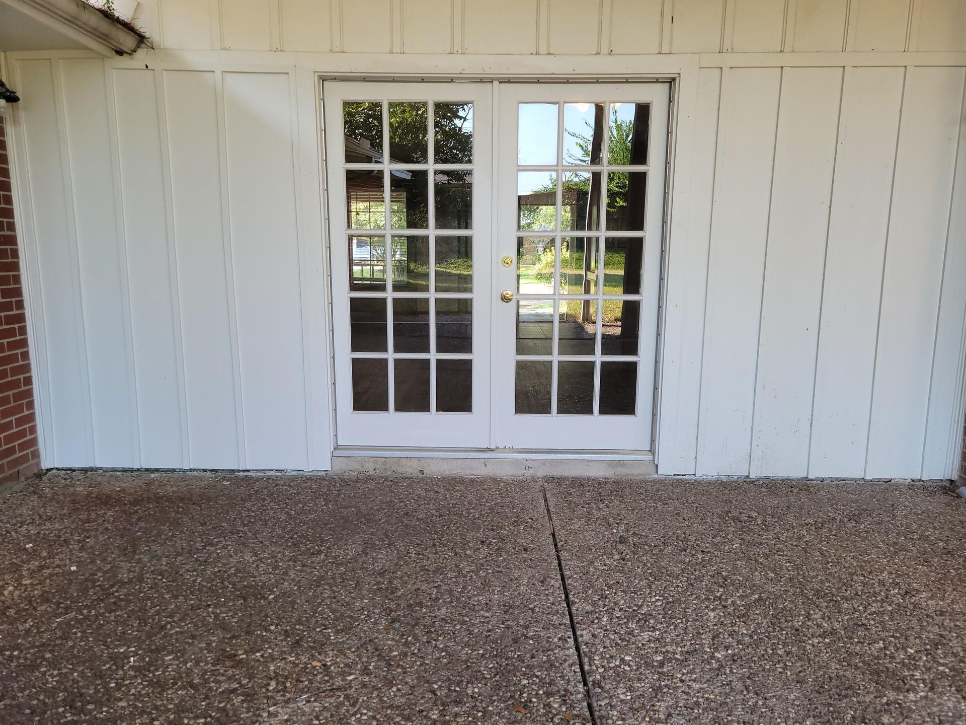 White French doors with multiple panes, surrounded by white paneling, open onto a speckled concrete patio.