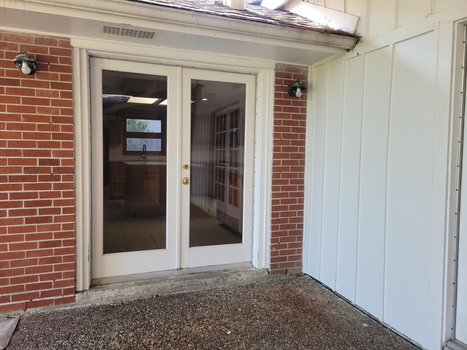 Glass double doors, red brick, white siding, and a stone-covered floor.