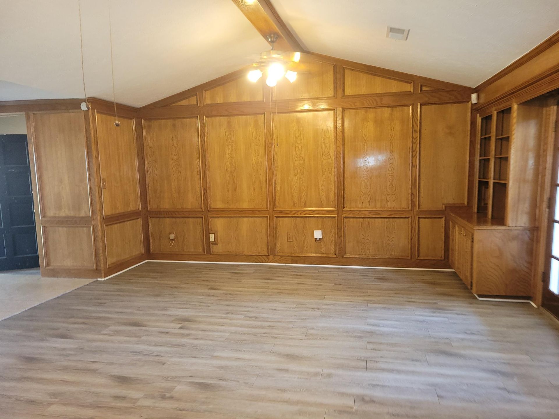 Empty room with wooden paneling on walls and ceiling. Light brown flooring.