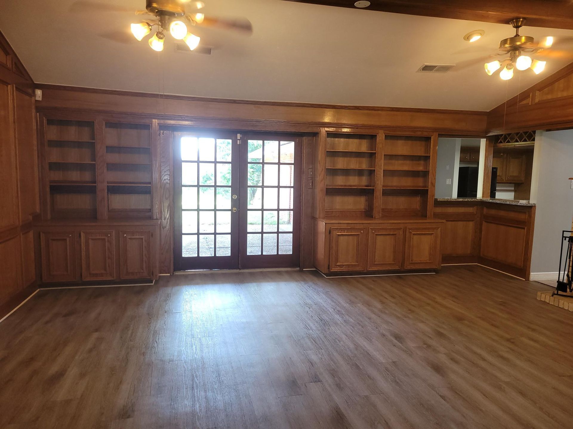 Empty living room with wood cabinets, built-in shelves, and double doors to outside.