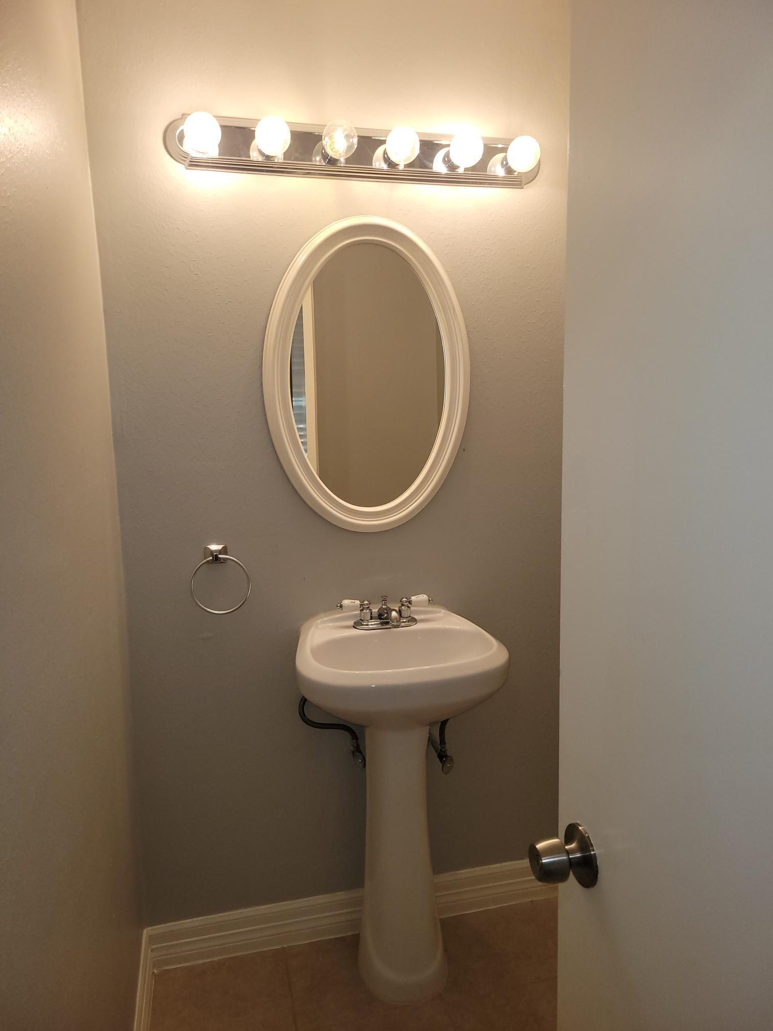 Small bathroom with pedestal sink, oval mirror, and overhead lighting.