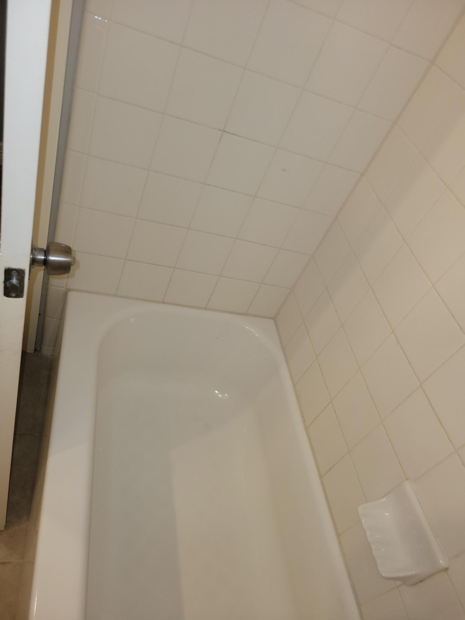 White bathtub in a bathroom with white tiled walls and ceiling. A door with a doorknob is on the left.