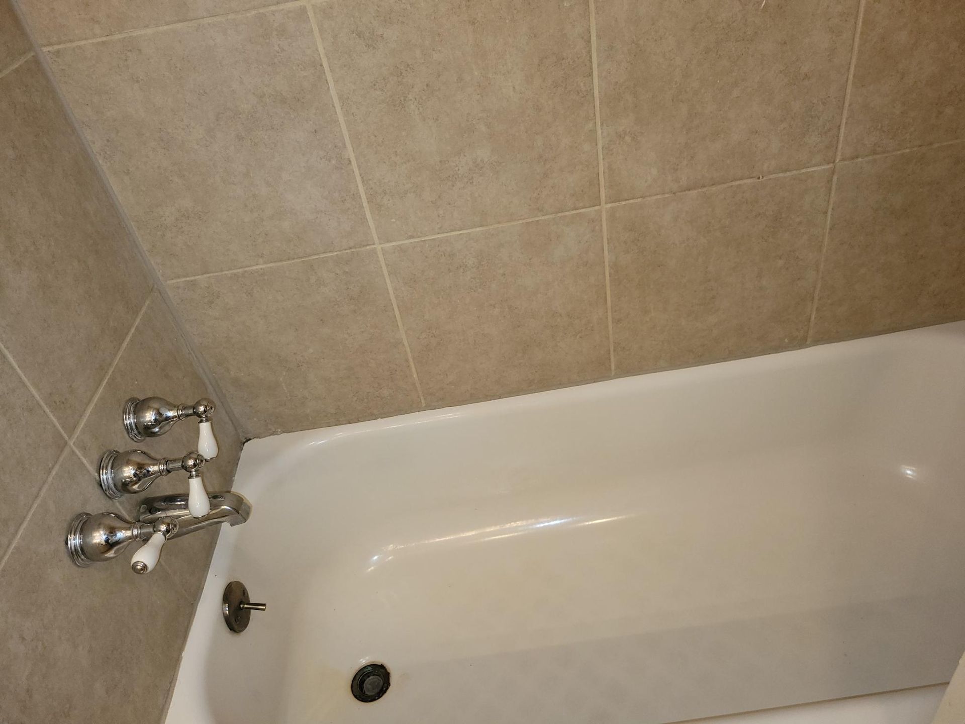 Bathtub with chrome fixtures, tan tile surround.
