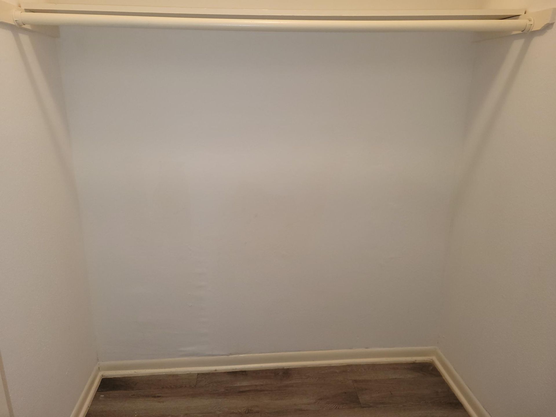 Empty closet with a clothing rod. White walls, wooden floor.