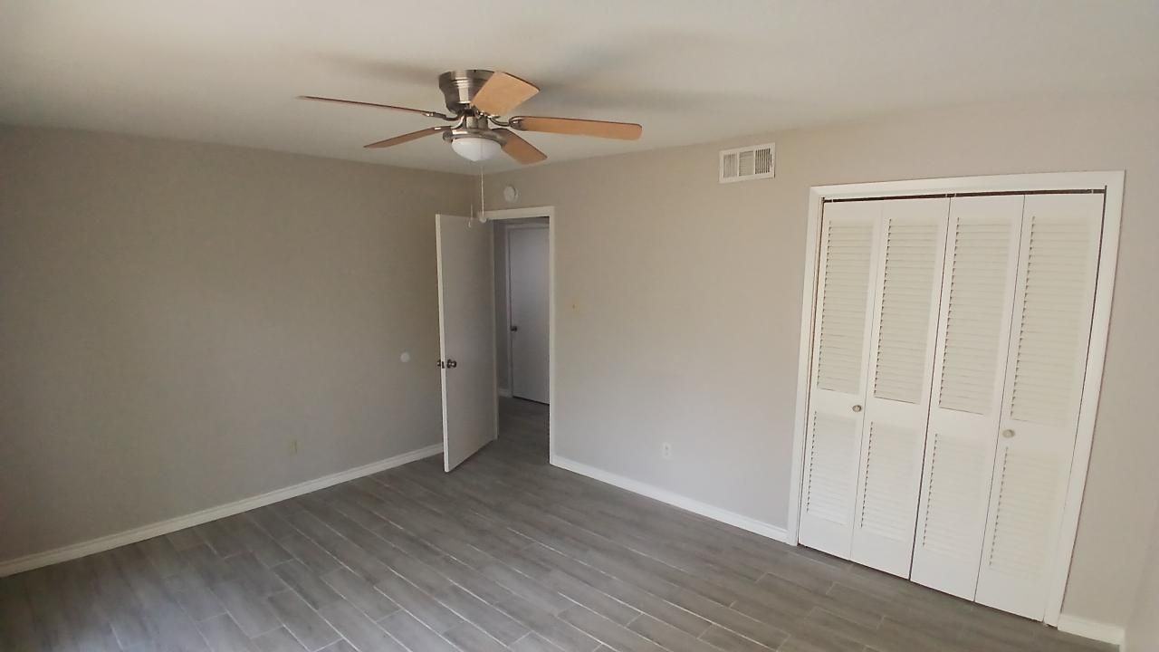 Bedroom interior with light gray walls, gray flooring, white closet doors, and a ceiling fan.
