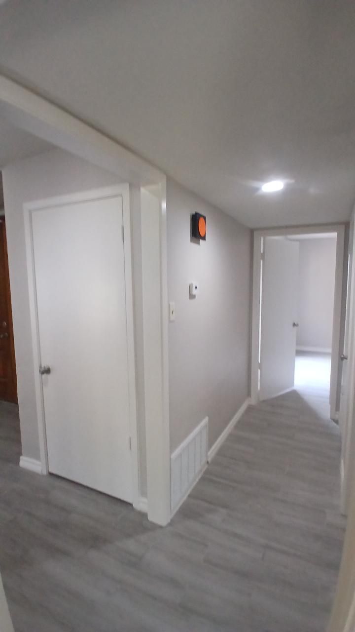 Hallway with white doors, light gray walls, and light wood-look flooring.