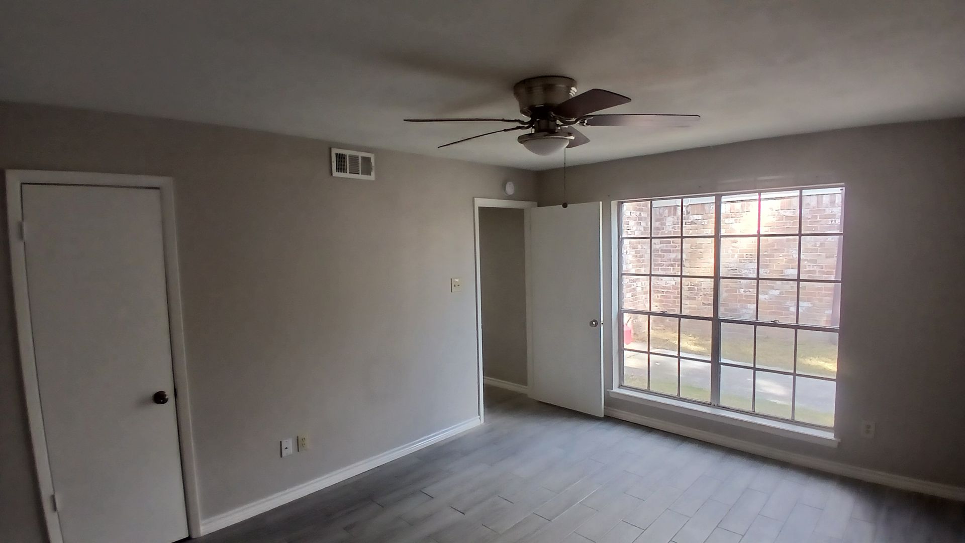Empty room with gray walls, dark wood-look floor, a window, doors, and ceiling fan.