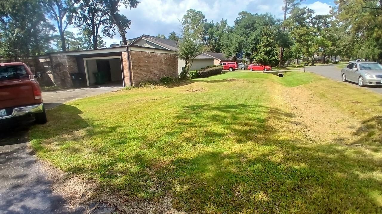 A suburban yard with a red truck parked in the driveway. The lawn is patchy with a slight ditch.