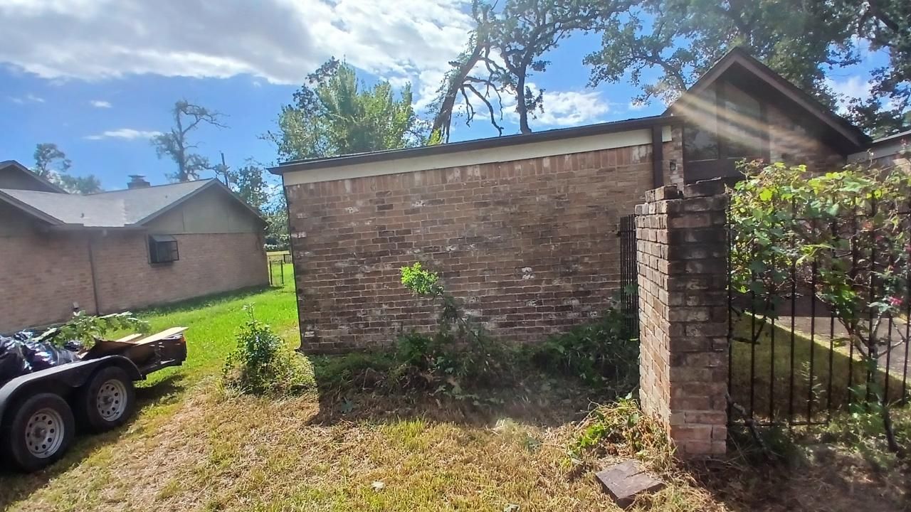 Brick wall and gate next to a house with a grass lawn, trailer parked nearby, sunny day.