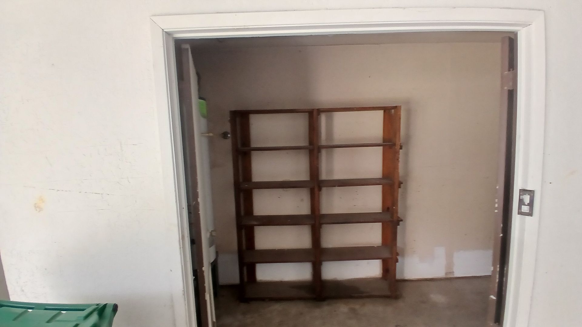 Open doorway revealing a room with a brown shelf against a light-colored wall.