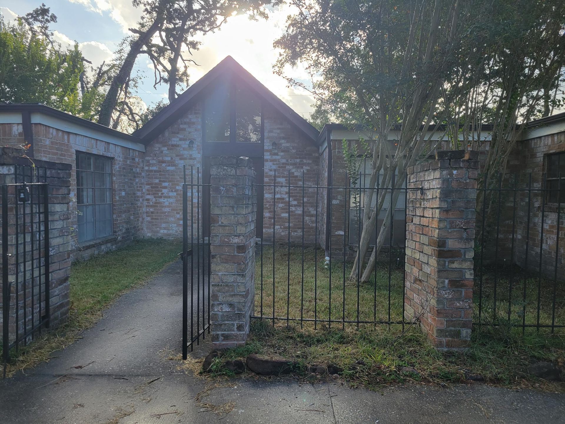 Brick building with a gated entrance and a paved walkway, surrounded by trees.