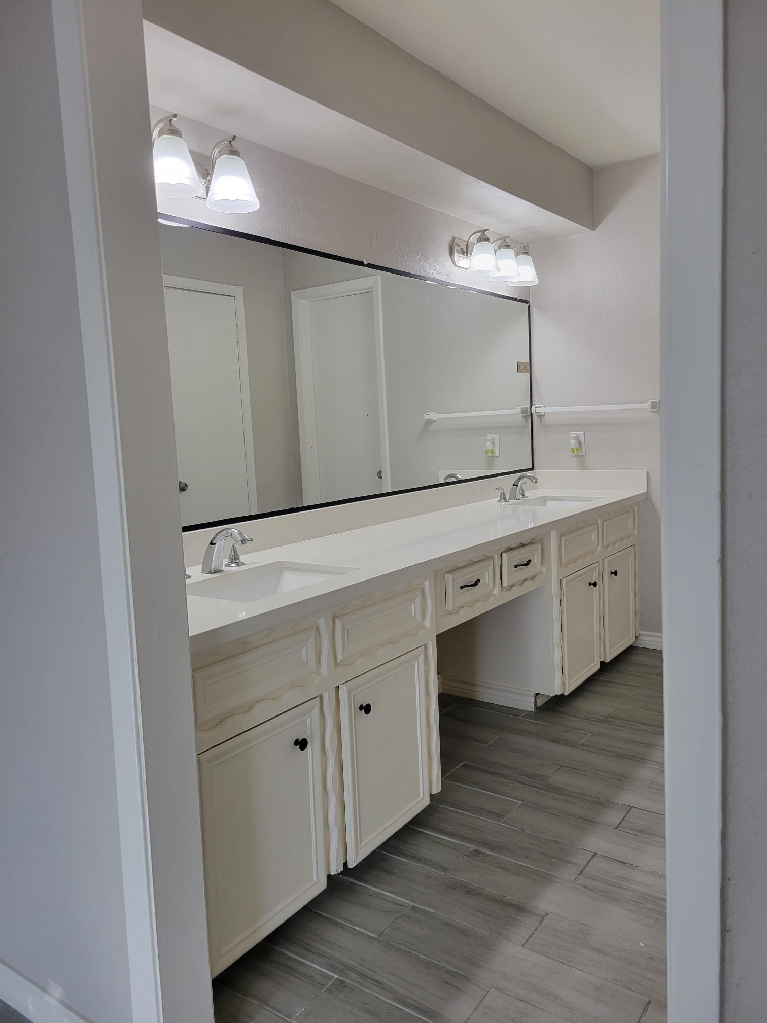 Bathroom with white cabinets, long mirror, and light fixtures. Gray flooring.