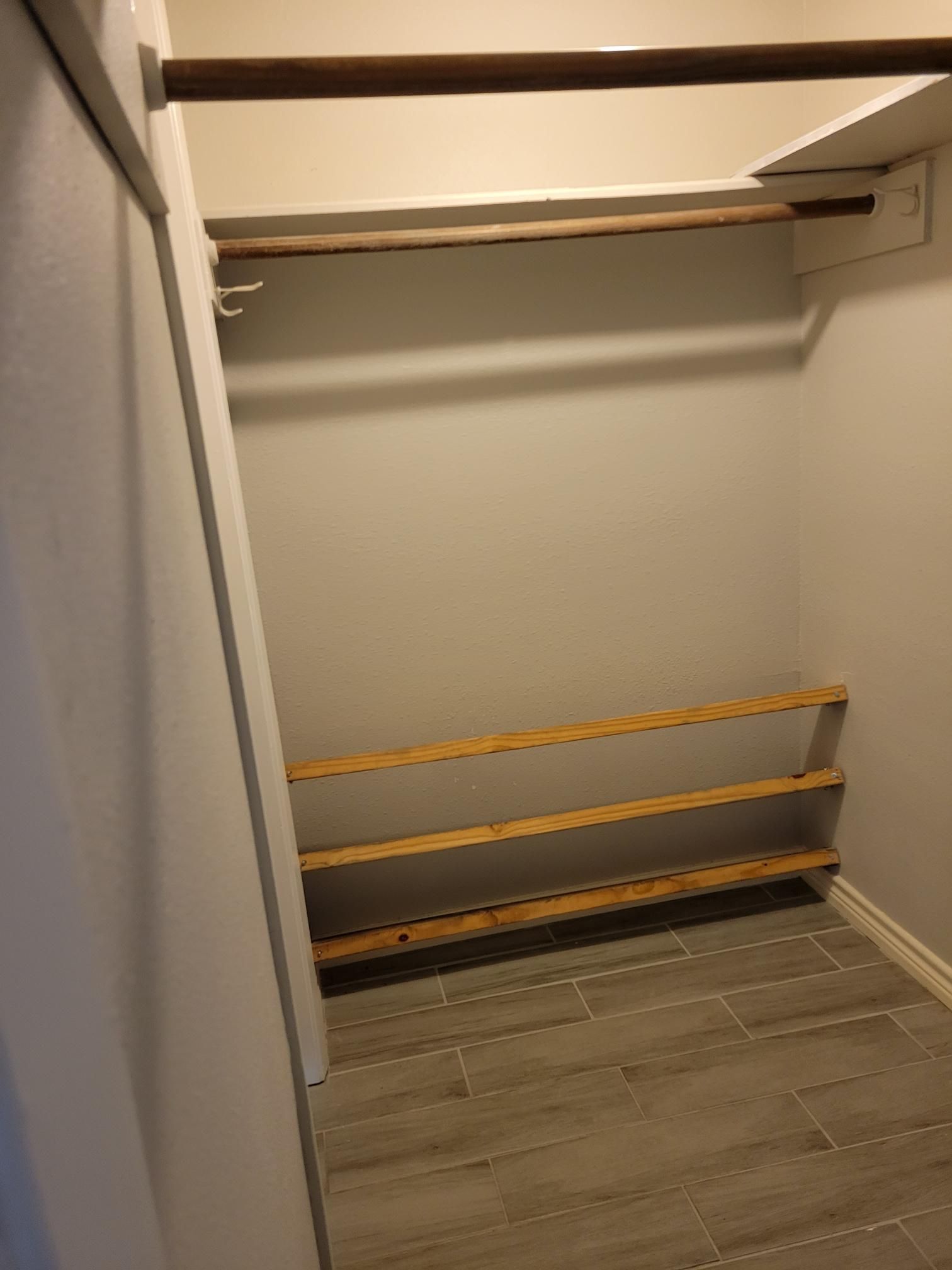 Empty closet with shelves, a hanging rod, and a tiled floor. Beige and white colors.