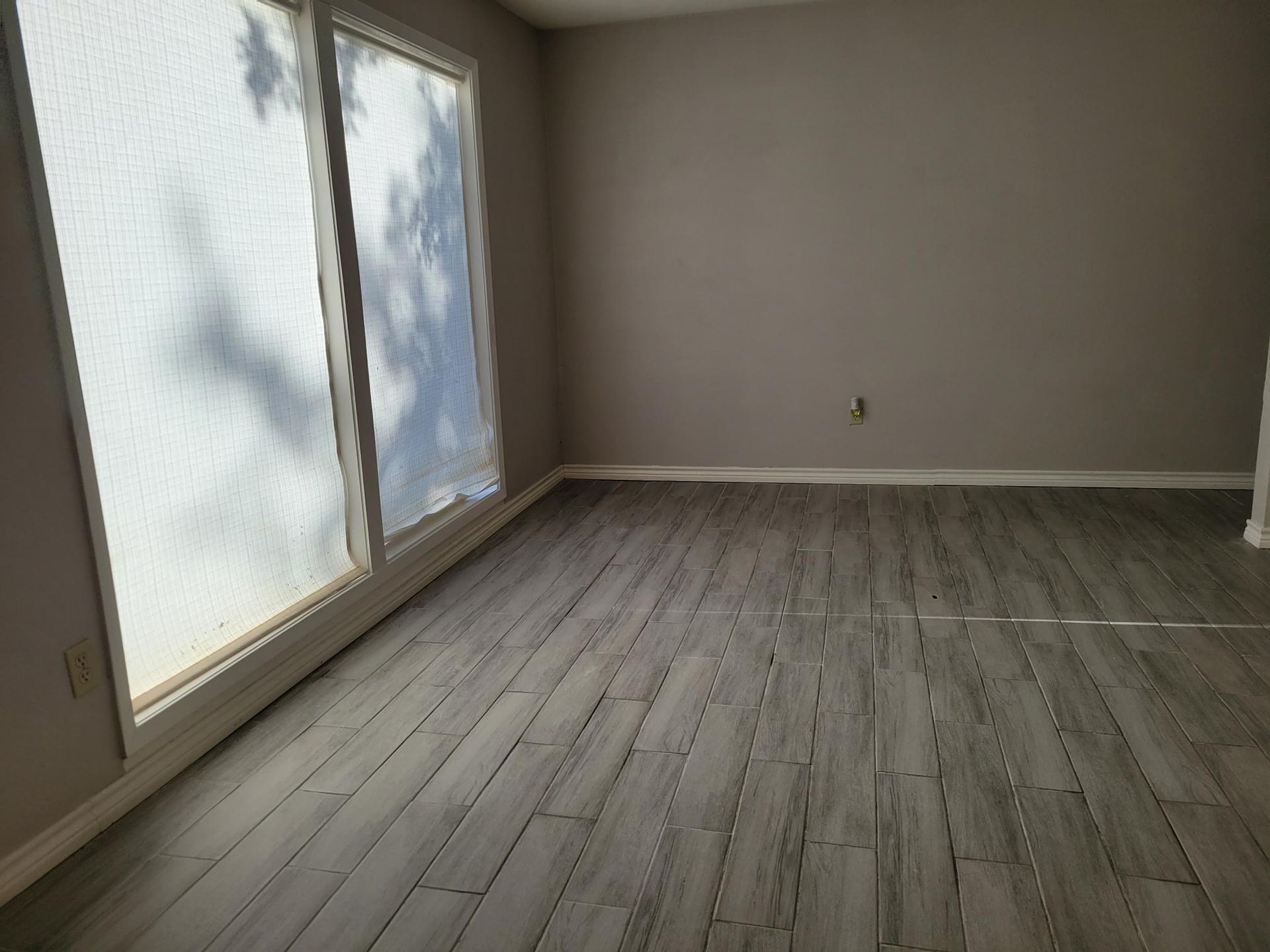 Empty room with wood-look flooring and a large window covered in a light shade. Gray walls and white trim.