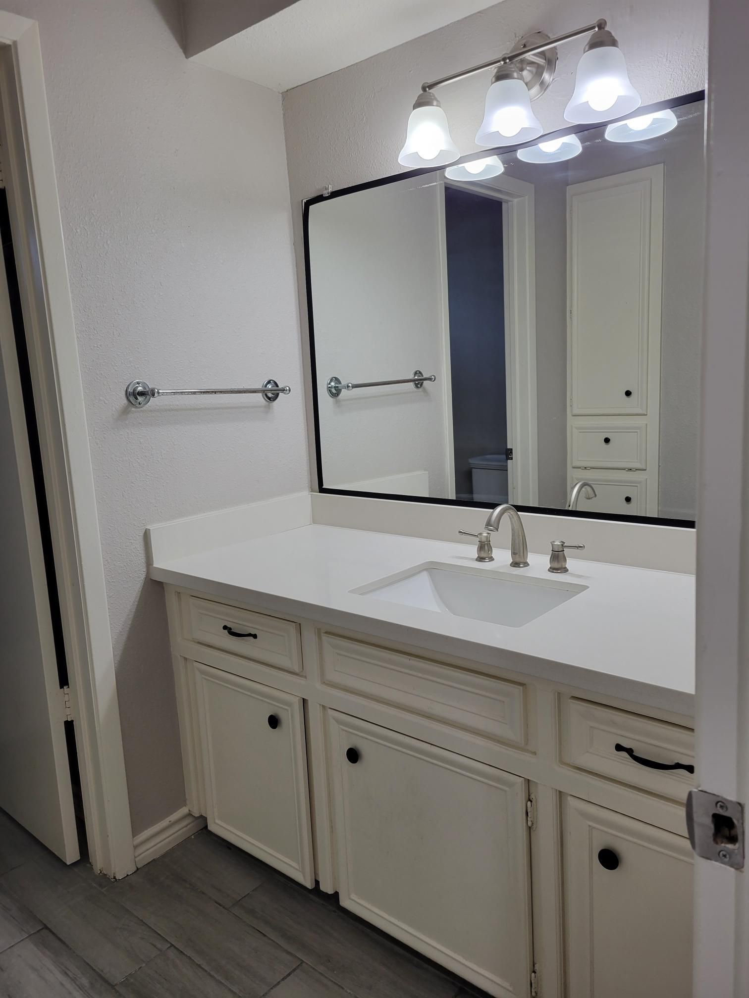 Bathroom with white vanity, large mirror, and overhead lighting.  Towel bar on the left.