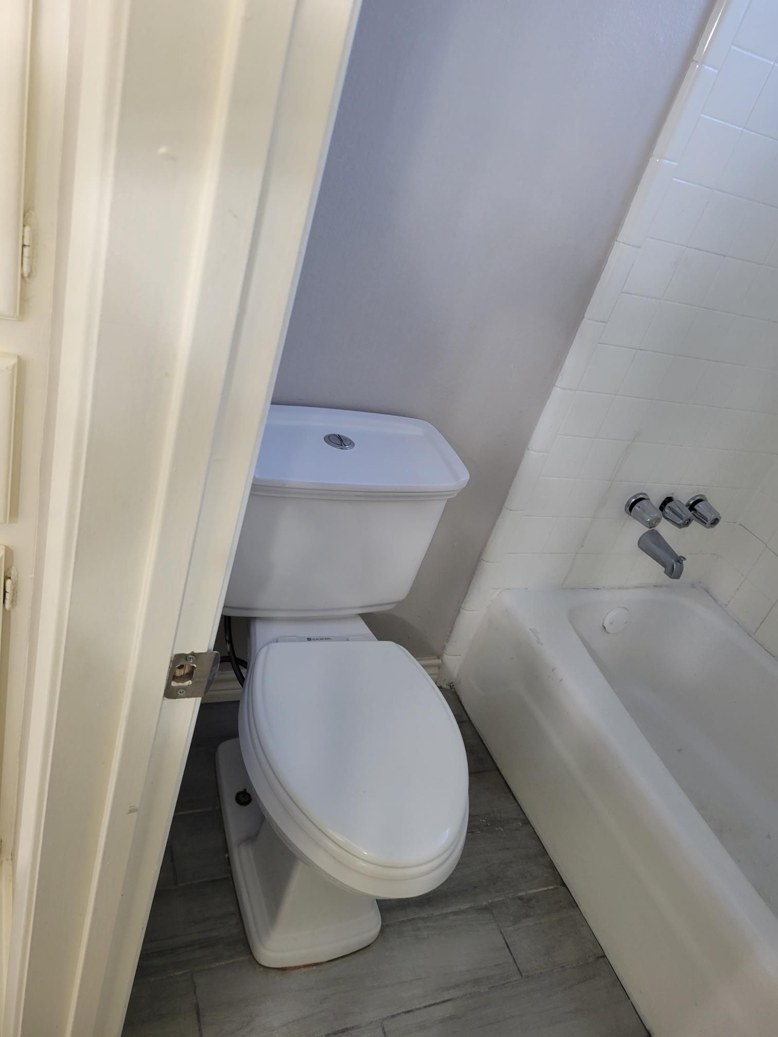 Bathroom with toilet and partially visible bathtub; white, angled walls.