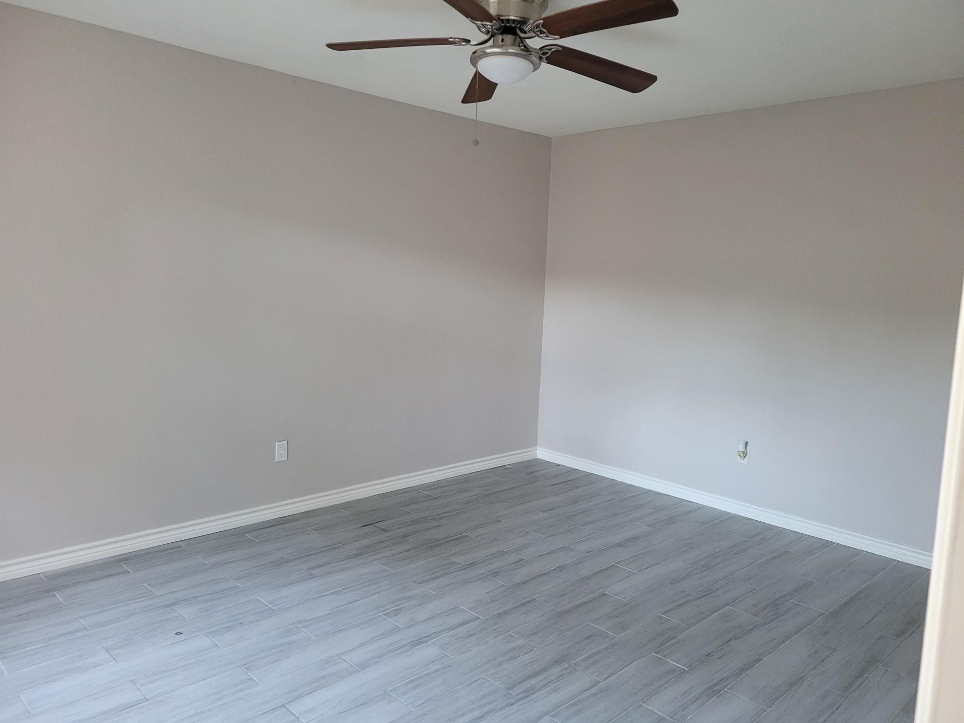 Empty room with gray flooring, light purple walls, white trim, and a ceiling fan.