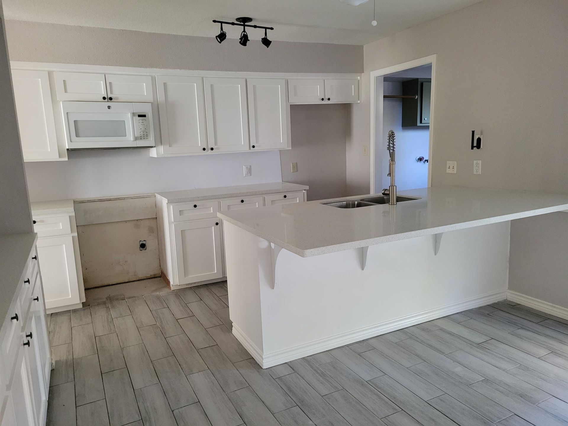 White kitchen with cabinets, countertops, and a central island on gray wood-look flooring.
