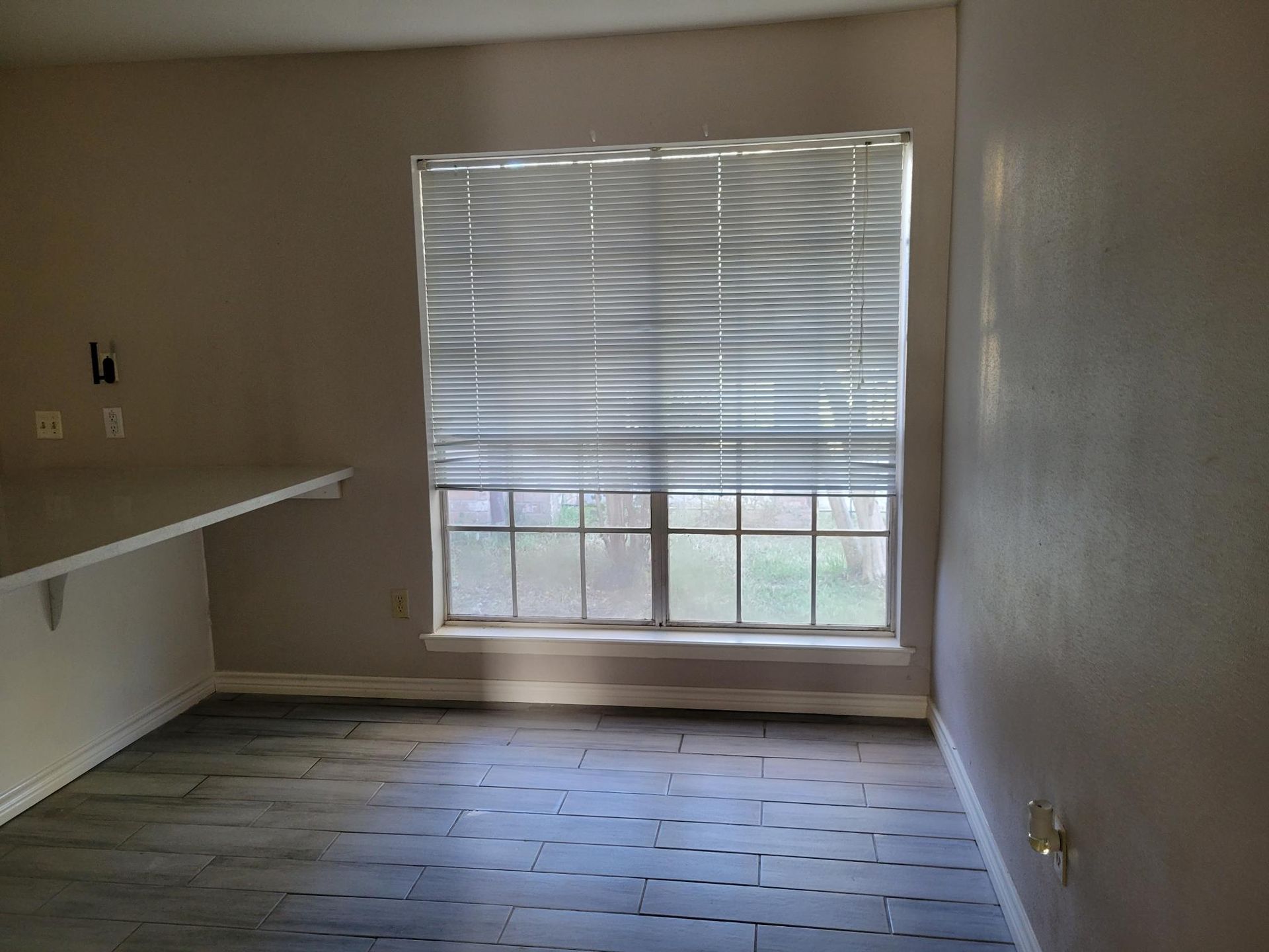 Room with gray flooring, window with blinds, and a white counter. Beige walls.