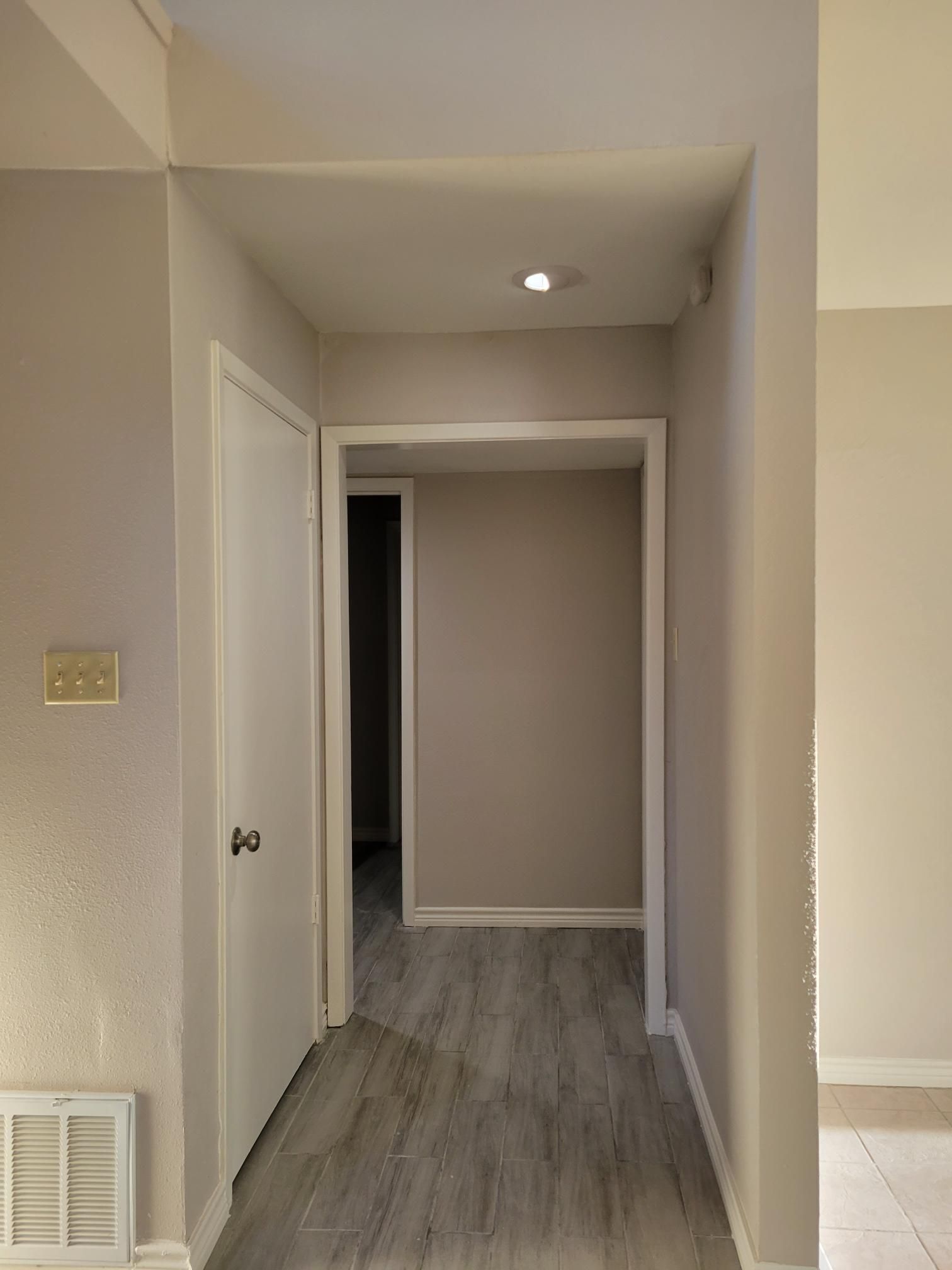 Hallway with a door on the left and doorway ahead. Light gray walls, light wood-look floor.