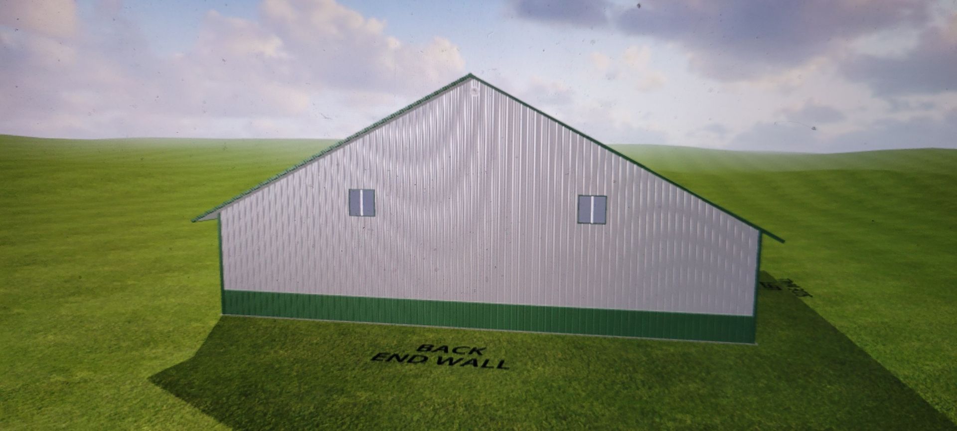 Back of a silver barn with two windows and a green base, set in a grassy field under a cloudy sky.